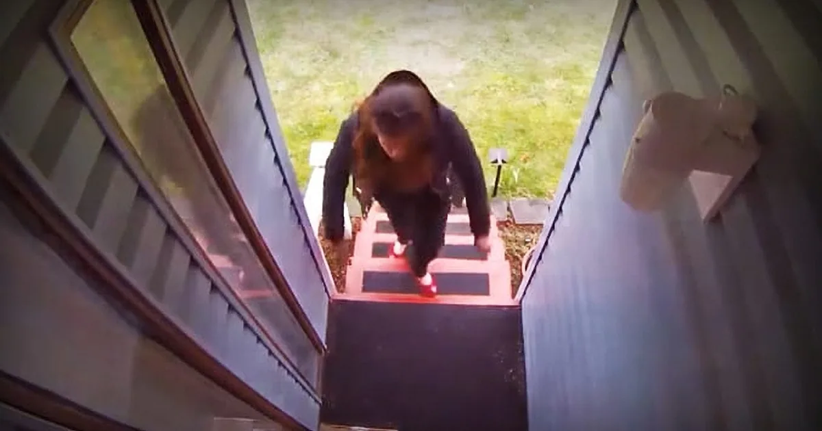 A person with long hair descends a staircase, illuminated by a red light at the bottom.