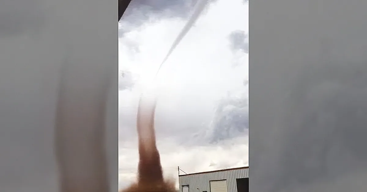 A tornado is forming, with a funnel cloud extending from the sky towards the ground near a building.