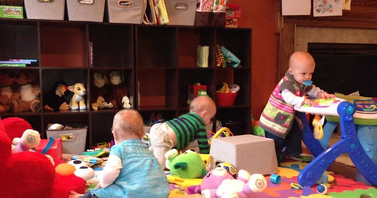 Three babies are playing with toys in a room filled with shelves and colorful items.