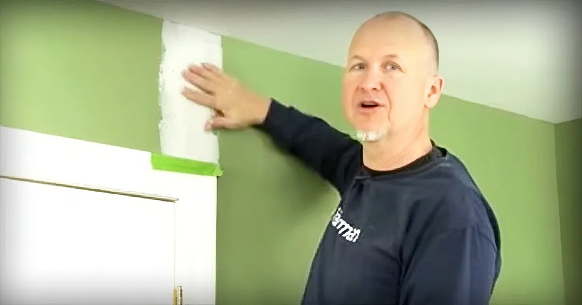 A man in a black shirt is painting a green wall with white paint.