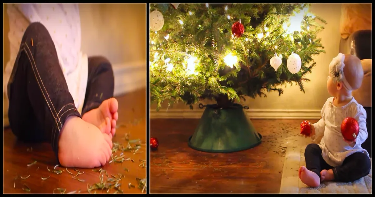 A baby sits on the floor, surrounded by fallen pine needles, near a Christmas tree with lights and ornaments.
