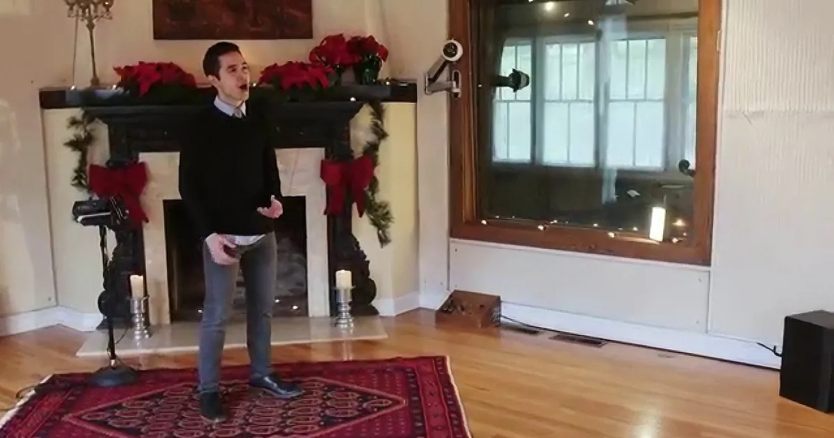 A man stands on a red rug in front of a fireplace decorated with Christmas ornaments.