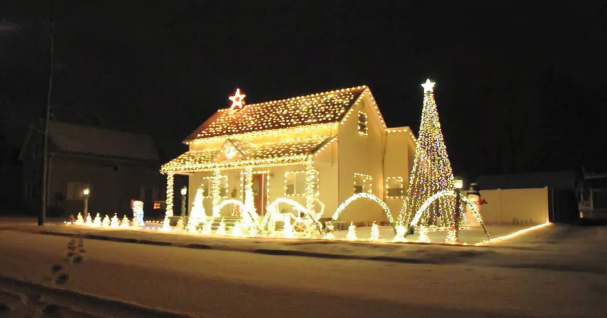 A house adorned with festive Christmas lights and decorations stands illuminated against a snowy night.