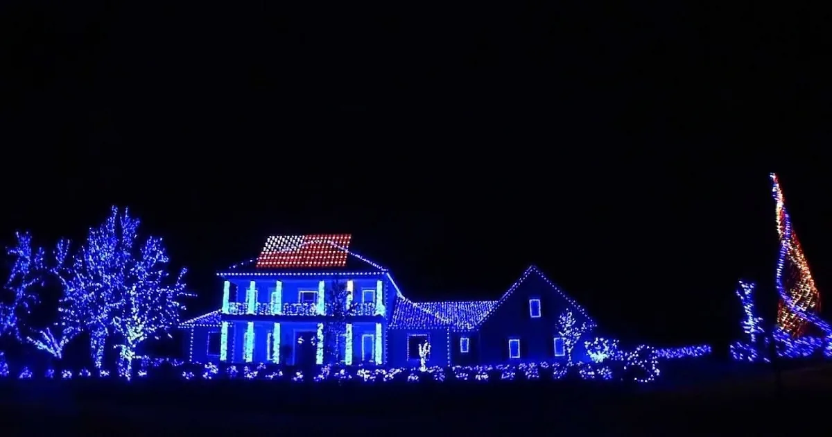 A house adorned with blue lights and a red roof stands illuminated against a dark night sky.