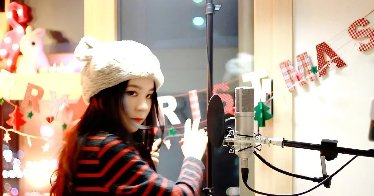 A person in a striped shirt and furry hat stands in front of a microphone, surrounded by festive decorations.