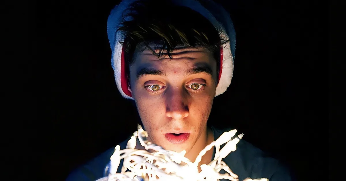 A person wearing a Santa hat with glowing eyes and a surprised expression, surrounded by white lights.