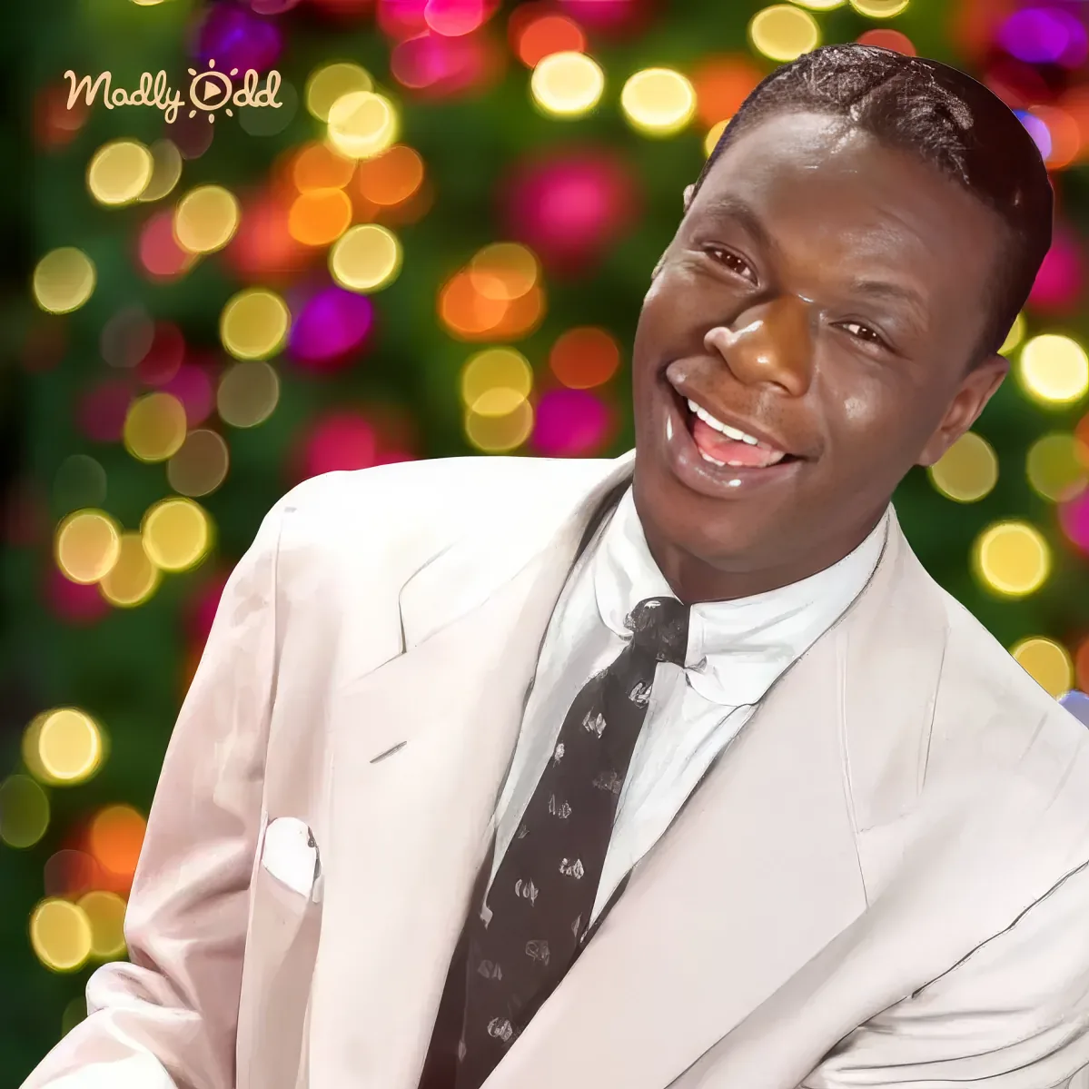 A man in a white suit and tie smiles against a colorful, bokeh-lit background.