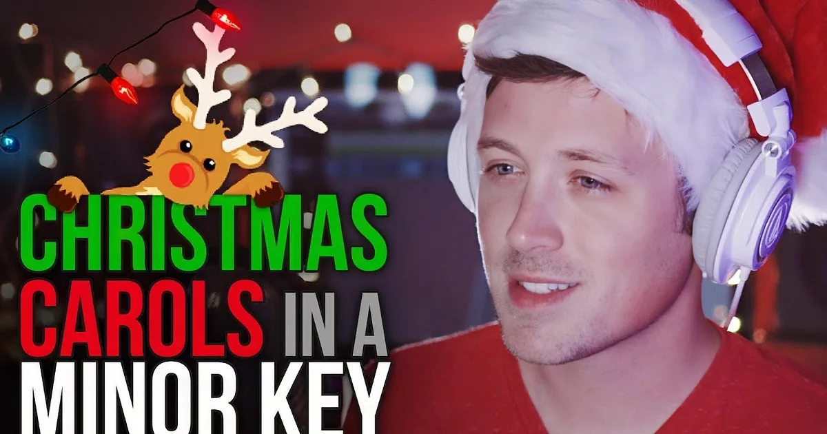 A person wearing a Santa hat and red shirt with headphones, standing in front of speakers and string lights.