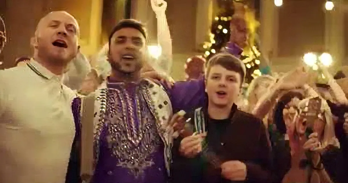 A man in a purple traditional outfit sings passionately with others in a festive setting.