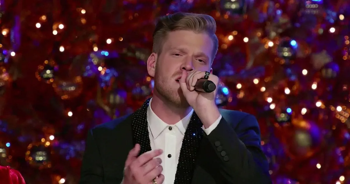 A man in a suit sings into a microphone, surrounded by festive lights and ornaments.