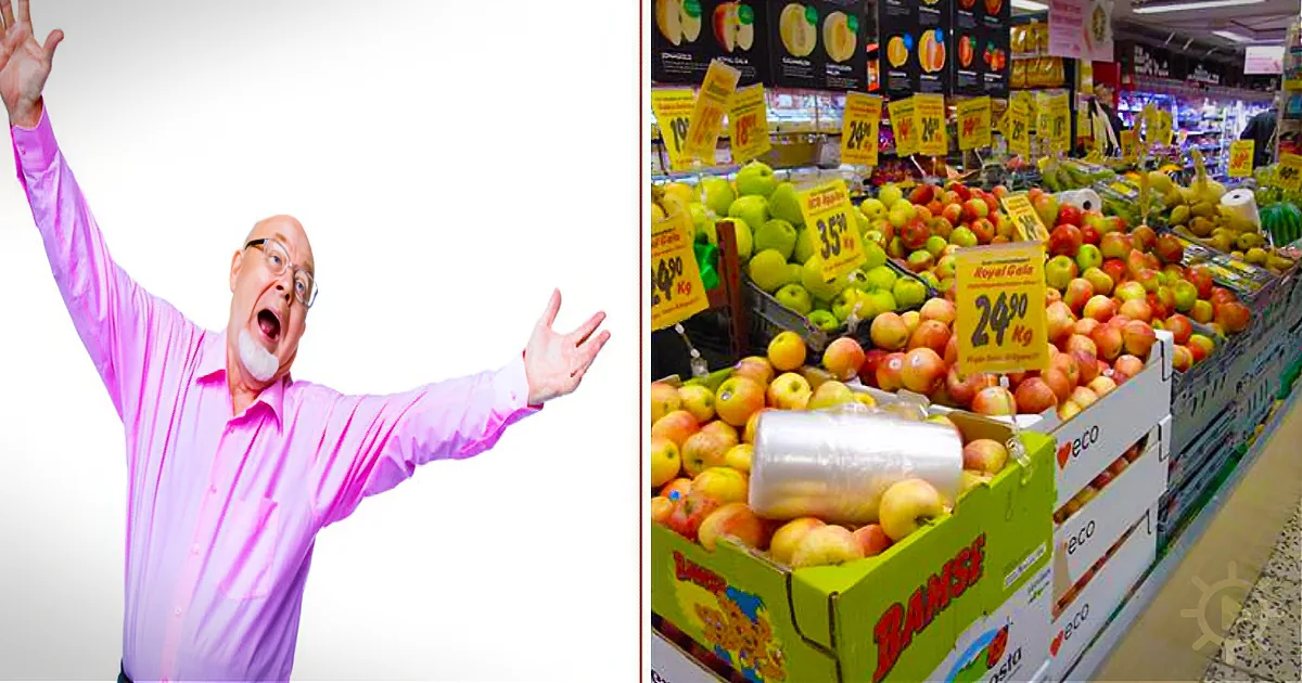 A man in a pink shirt is excitedly raising his arms in front of a grocery store fruit section.
