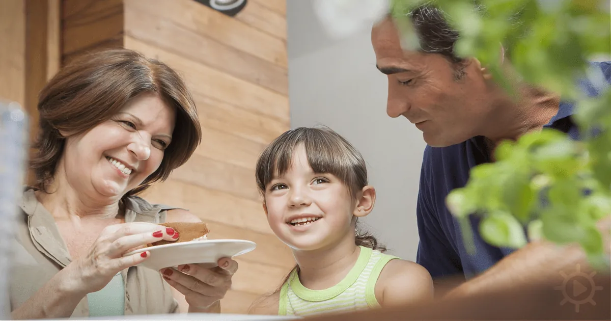 A smiling family of three enjoys a meal together, with a woman holding a sandwich.