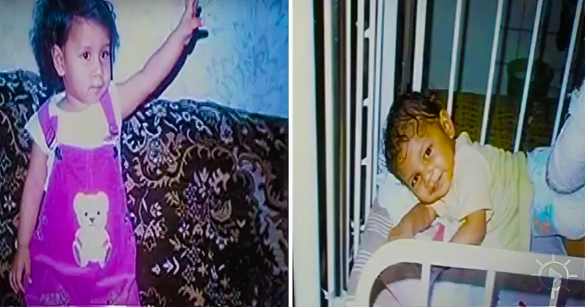 A child in a pink dress stands on a couch, raising a hand, while another child lies in a crib, looking up.