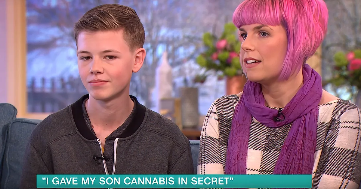 A young boy and a woman with pink hair are sitting on a couch, seemingly discussing a serious topic.