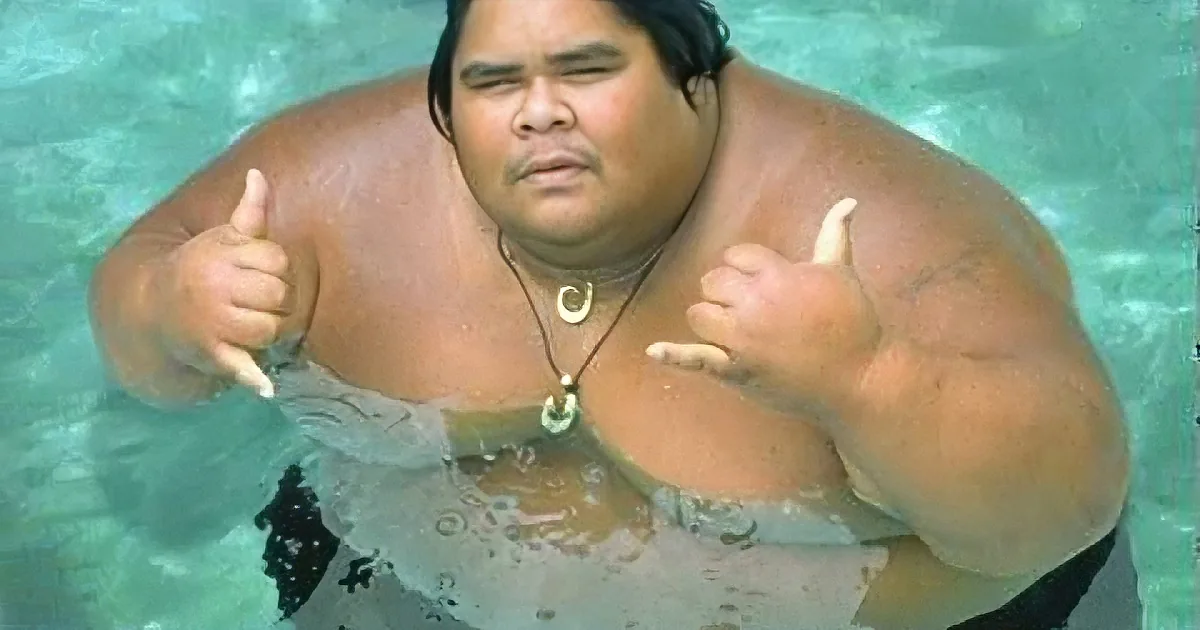 A person in a pool giving a thumbs-up gesture, wearing a necklace and a white garment.