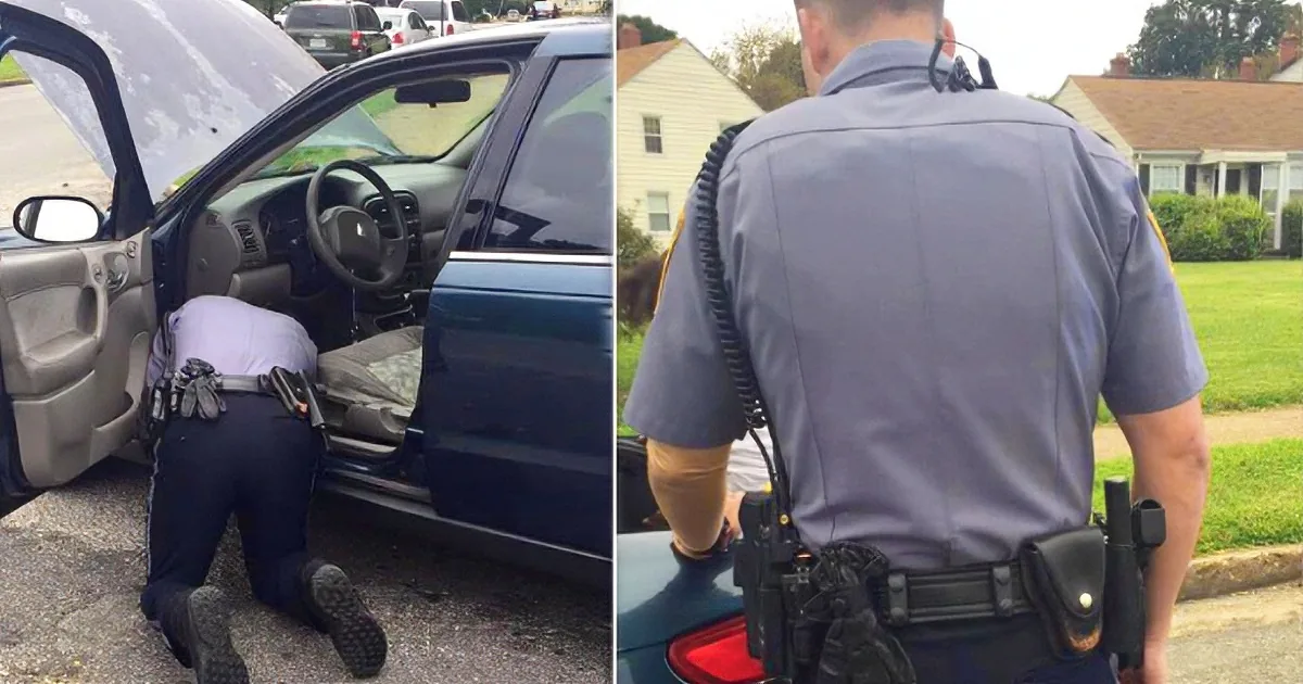A police officer is seen from the back, wearing a uniform and equipment, interacting with a car in a suburban setting.