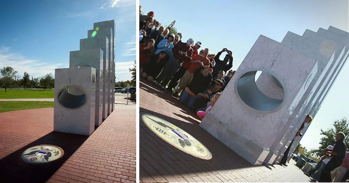 A modern sculpture with circular cutouts stands on a brick plaza, surrounded by a crowd of people.