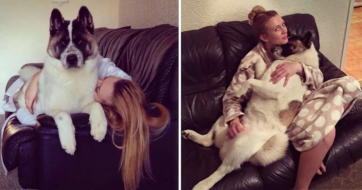 A woman in pajamas cuddles a large dog on a black leather couch.