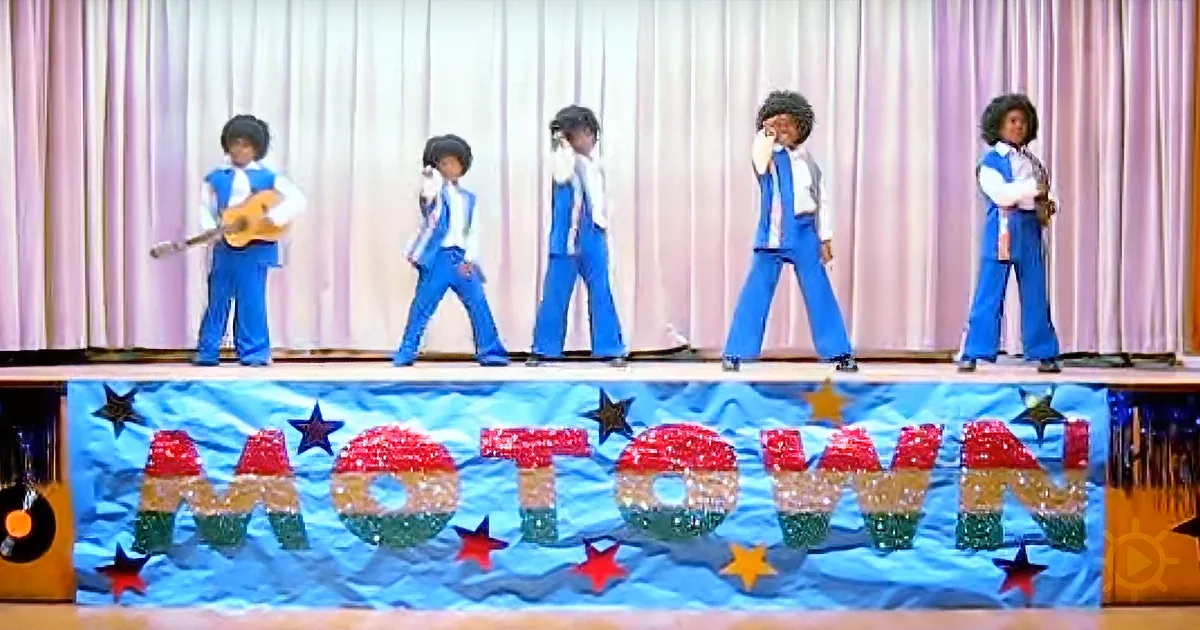Five performers in blue outfits on stage with a "Motown" banner and stars.