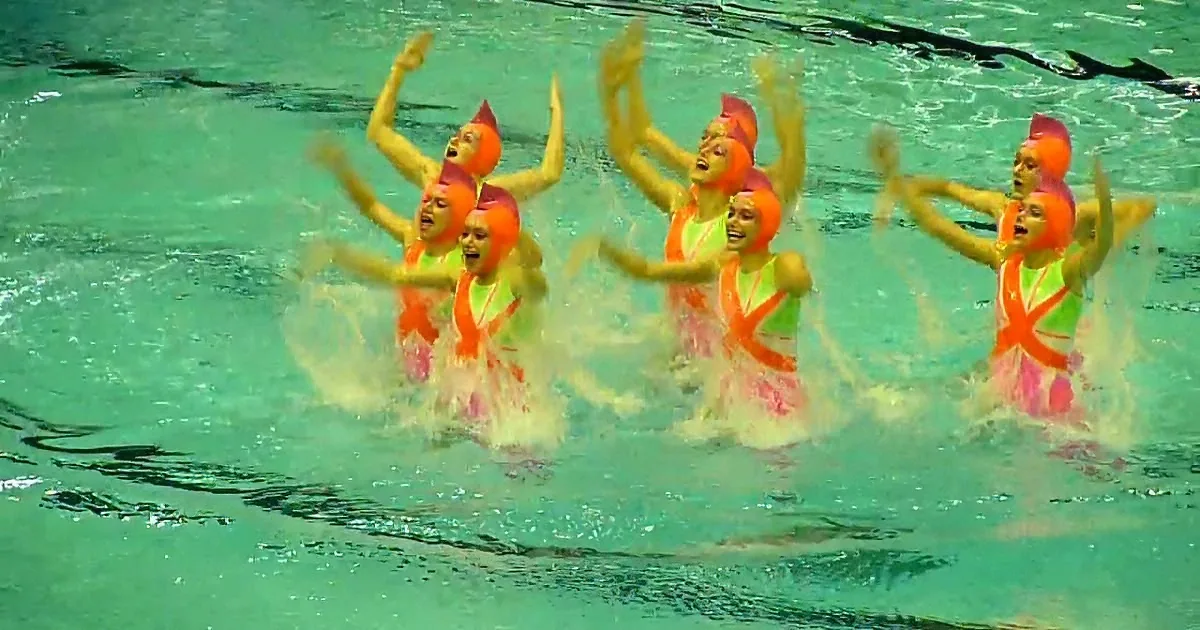 A synchronized swimming team in vibrant costumes performs a coordinated routine in a pool.