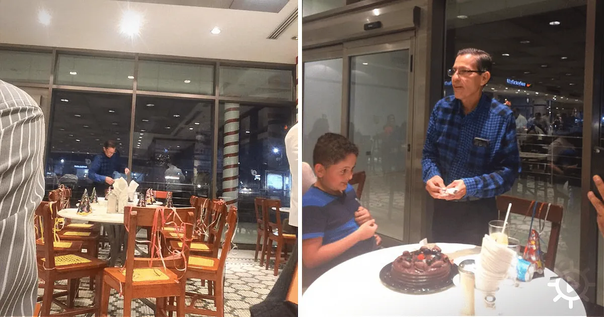 A man in a blue shirt stands by a boy at a table with a chocolate cake in a restaurant.