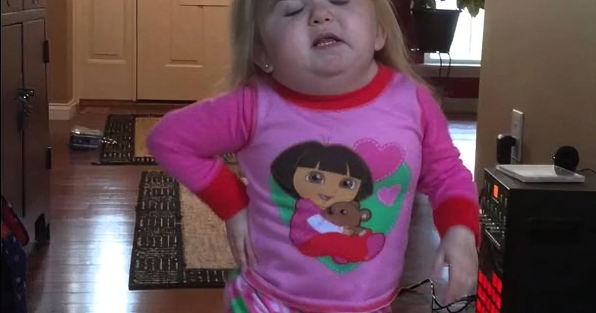A young child in pink Dora the Explorer pajamas stands in a kitchen, mouth open, looking up.