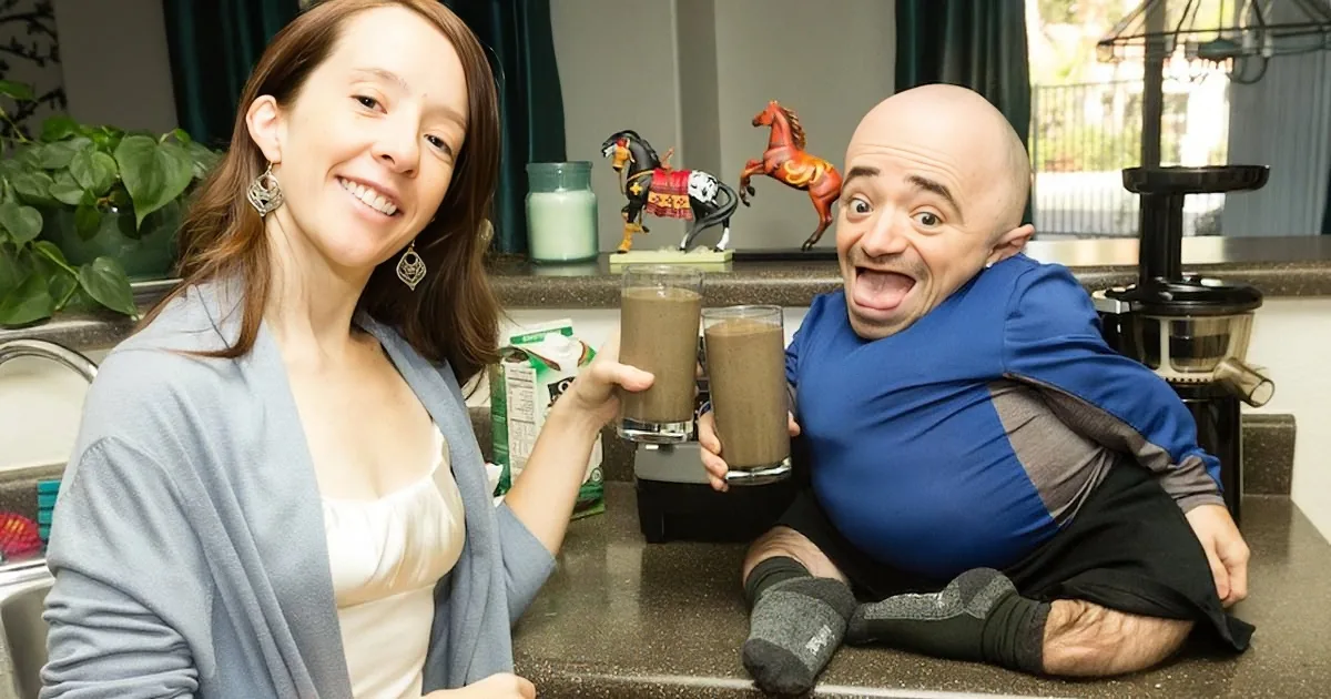 A woman and a man are holding smoothies, smiling, with a juicer and decorative horses in the background.
