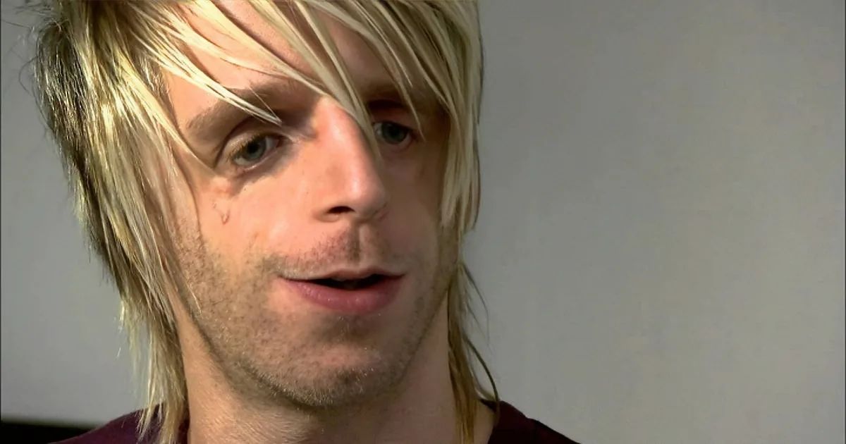 A person with long, light blonde hair and a maroon shirt is shown in a close-up shot.