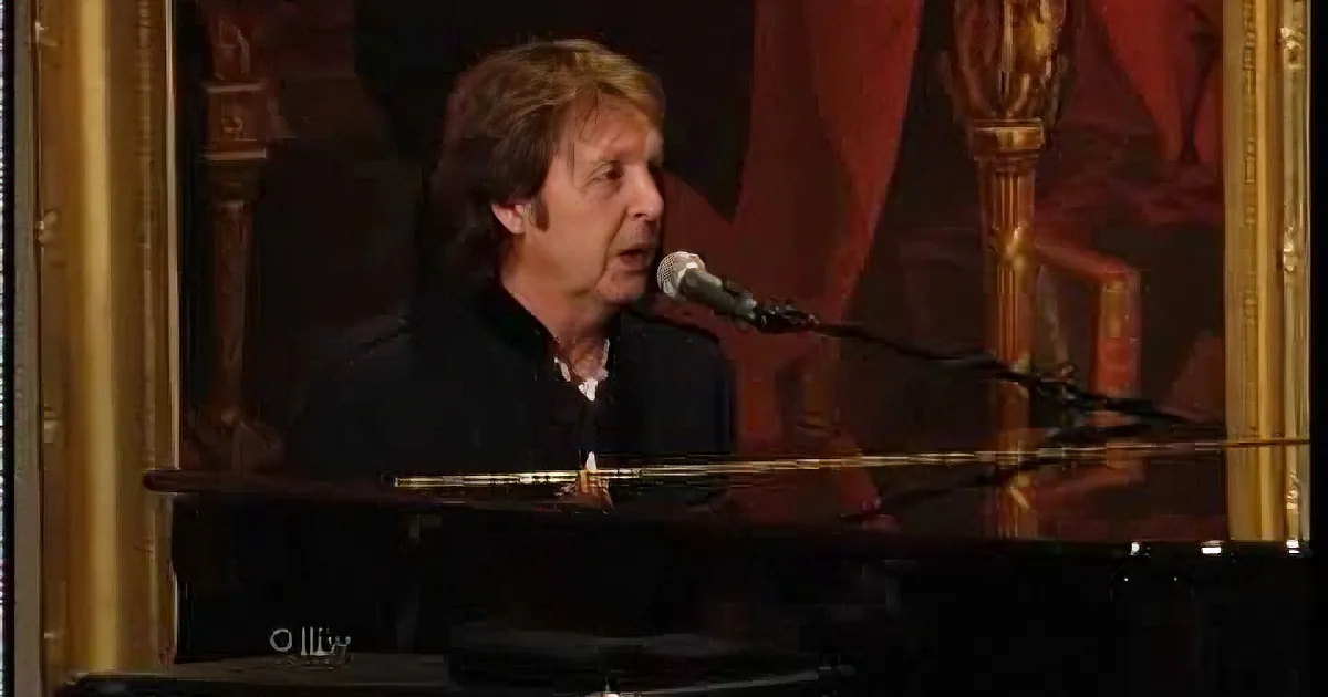 A man sings into a microphone while playing piano in a dimly lit, ornate room.
