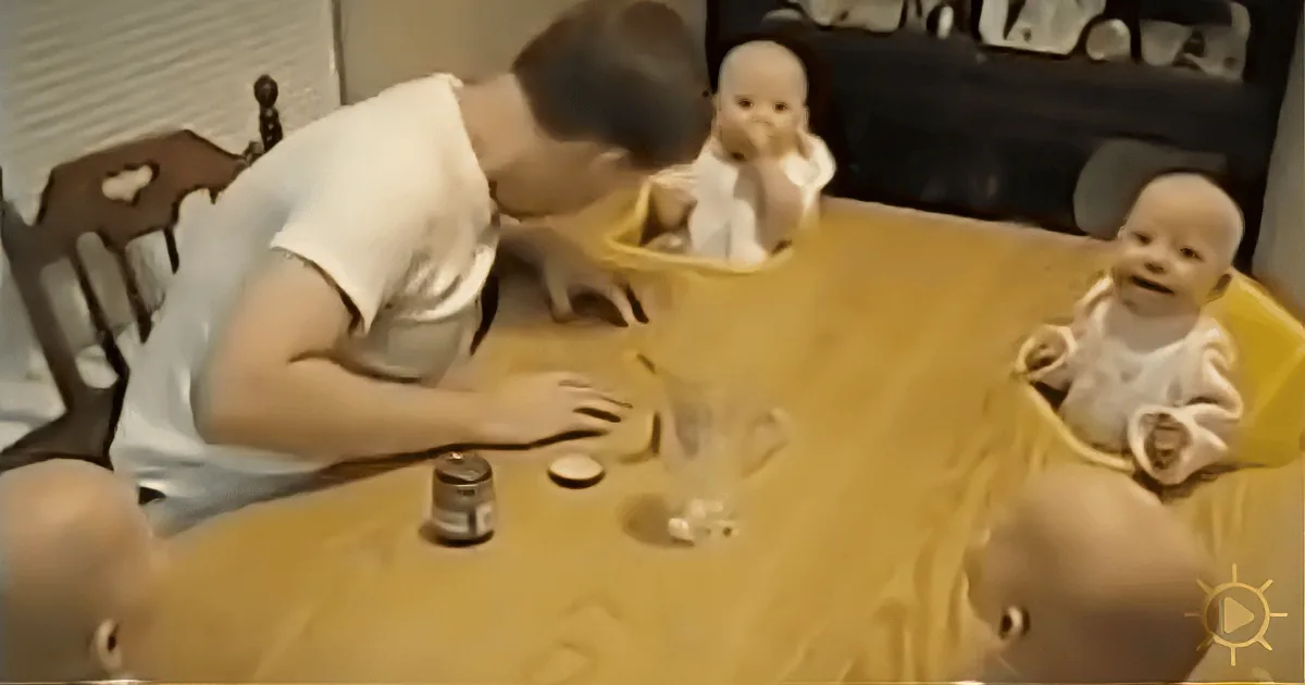 A person pours a drink into a glass on a table surrounded by baby dolls.