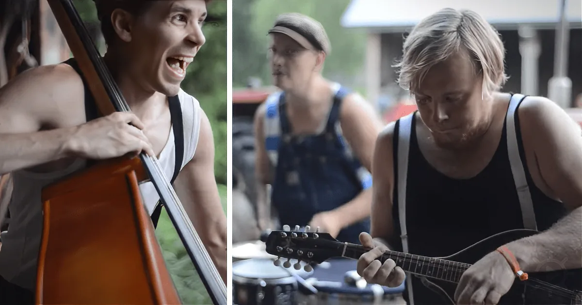 A man in a white tank top plays a cello with passion, while another man in overalls plays guitar nearby.