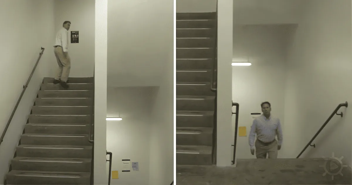 A man in a white shirt and khaki pants walks down a staircase in a dimly lit hallway.