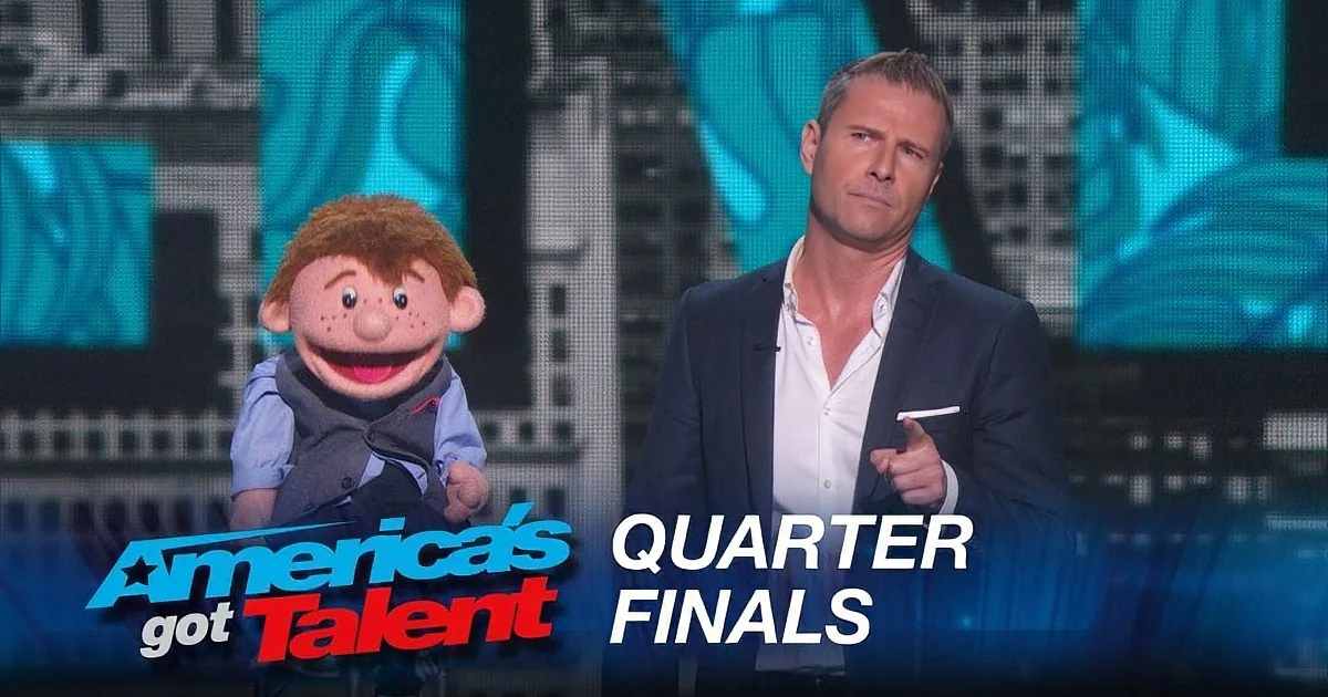 A man in a suit sits next to a puppet on stage at America's Got Talent Quarter Finals.