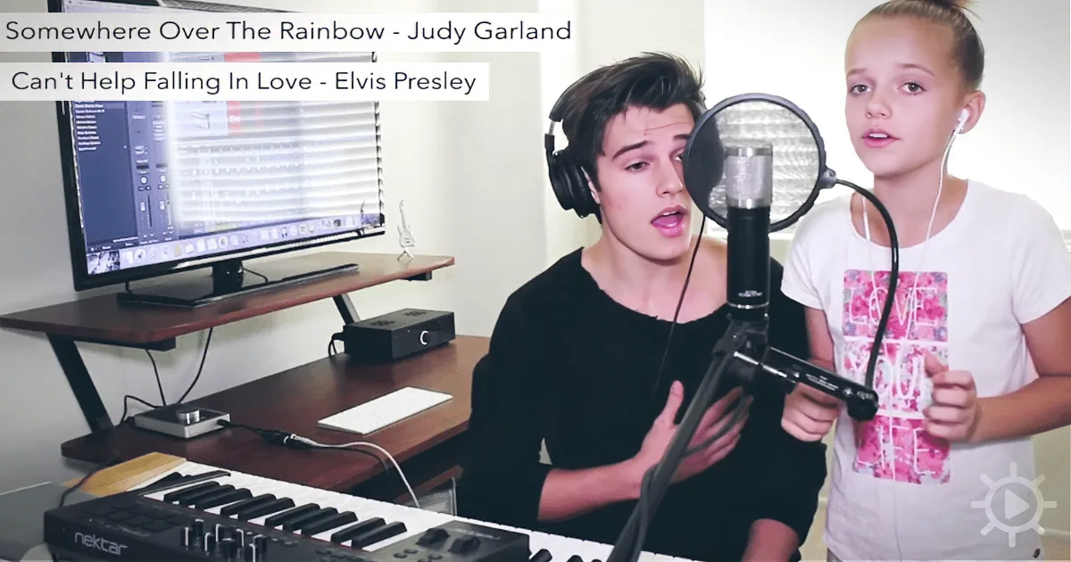 A young man and girl sing into microphones, with a keyboard and computer in the background.