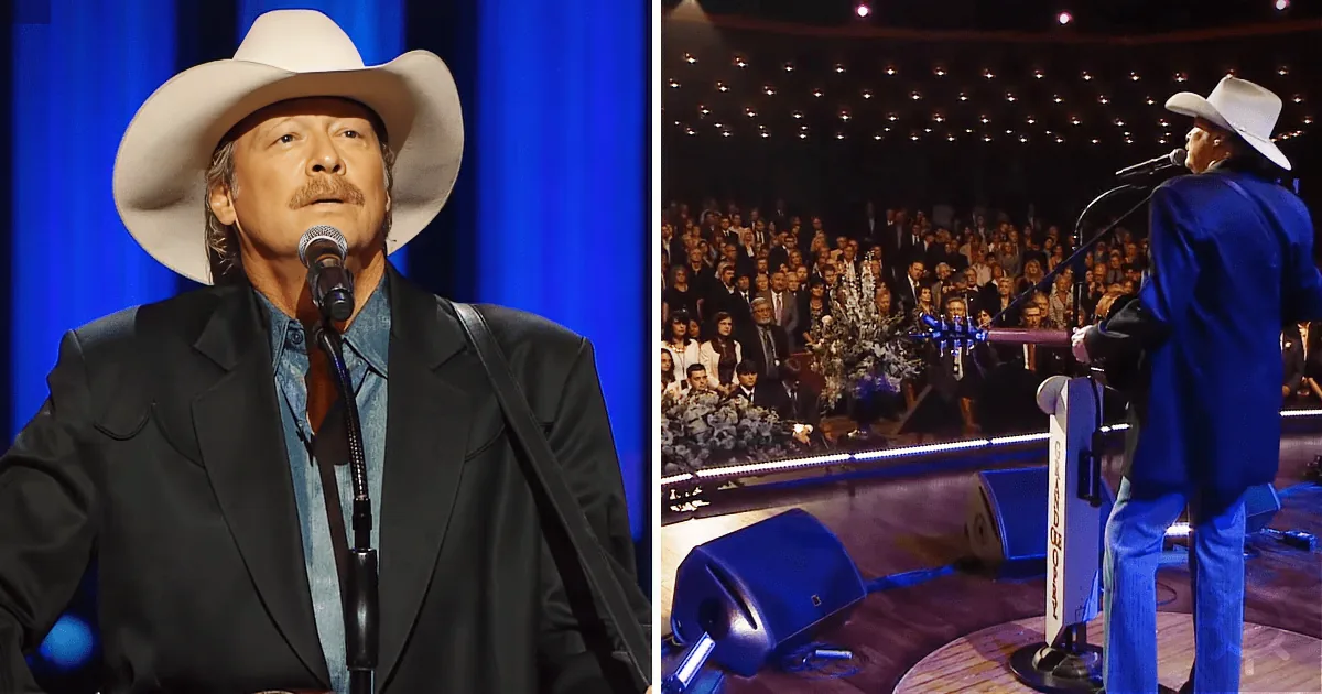 A man in a cowboy hat and suit sings into a microphone on stage, with a large audience in the background.