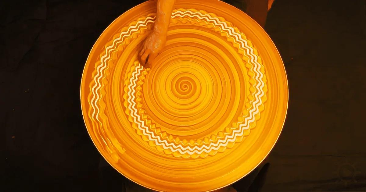 A person's hand spins a vibrant yellow plate with concentric circles and zigzag patterns on a dark surface.