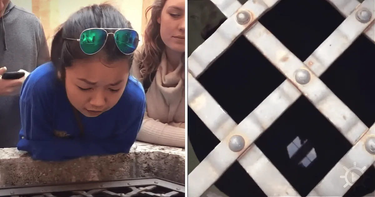 A young girl wearing sunglasses leans over a ledge, while a metal grate with a cross pattern is visible in the foreground.