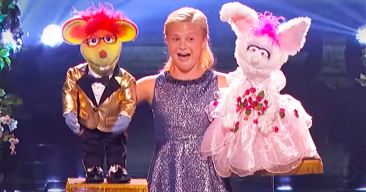 A person in a sparkly dress stands between two puppets, one in a tuxedo and the other in a floral dress.