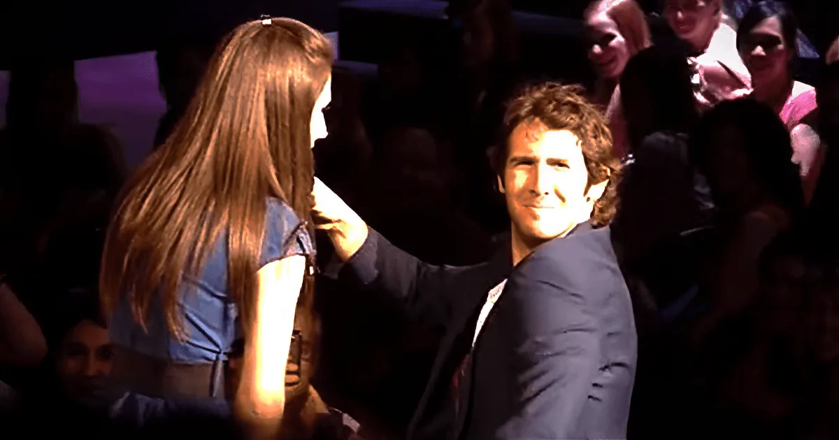 A woman with long blonde hair is dancing with a man in a suit in a crowded room.