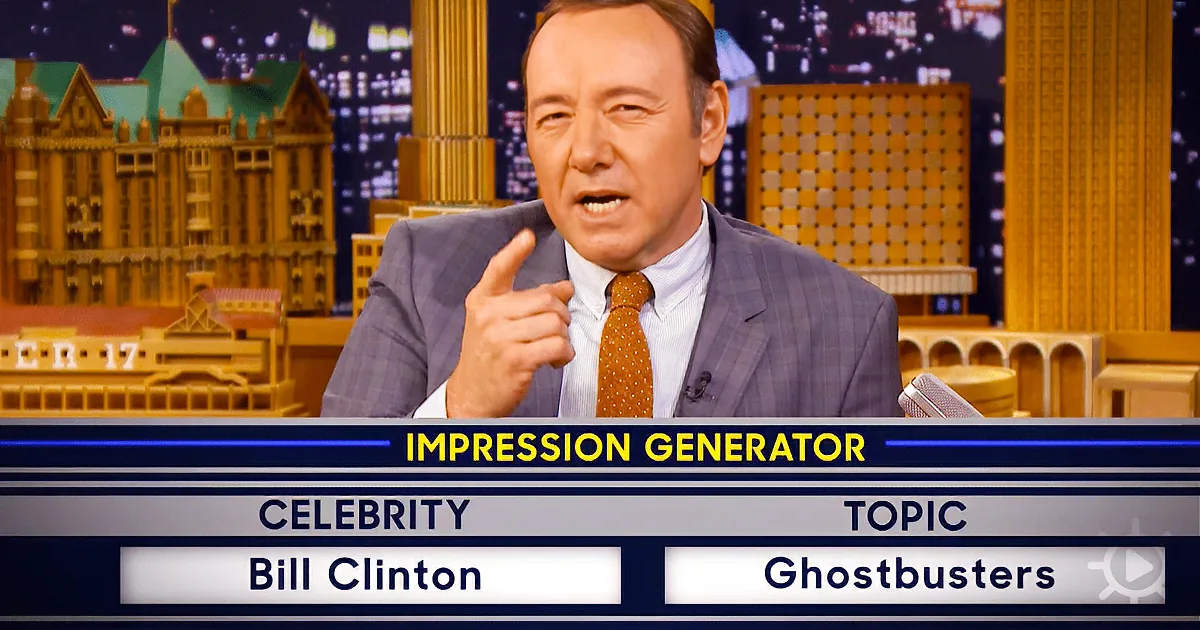 Kevin Spacey impersonates Bill Clinton on a talk show set with a cityscape backdrop.