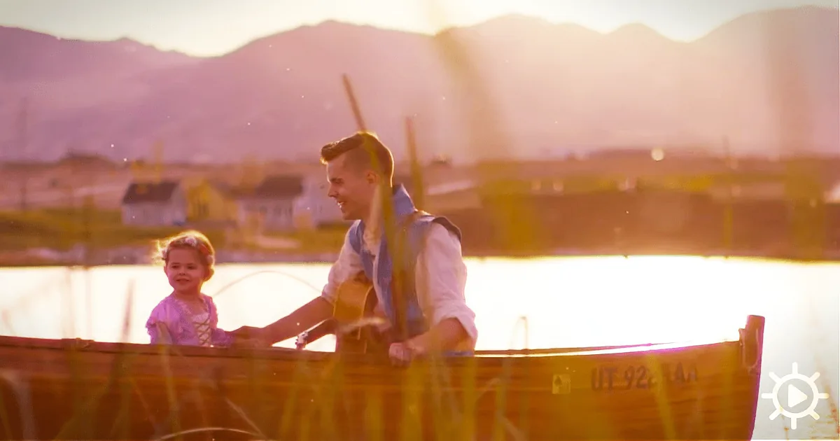 A boy and girl smile in a wooden boat on a serene lake, with mountains and warm sunlight in the background.