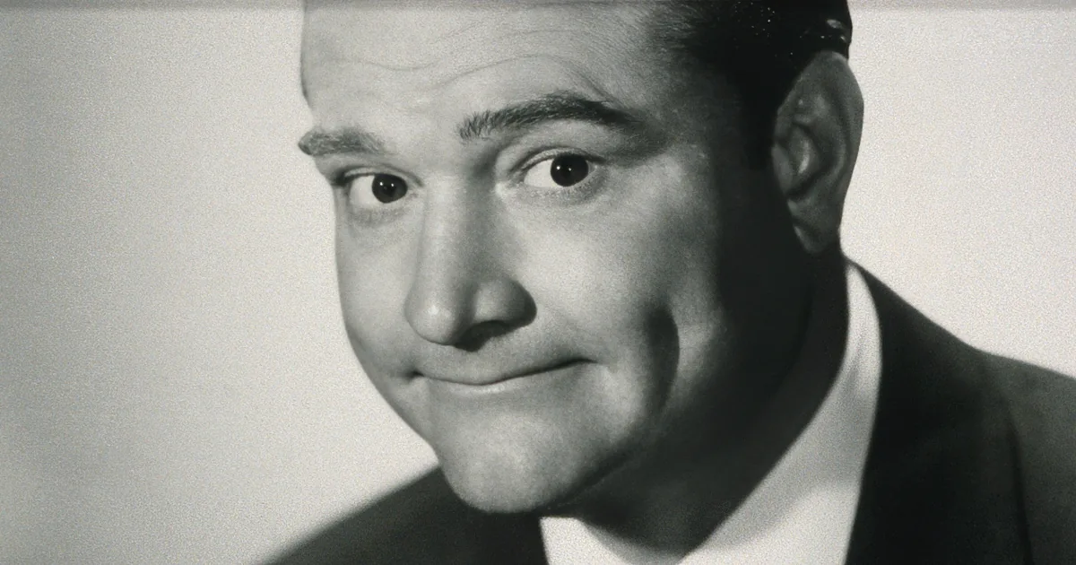 A man in a suit and tie is smiling with a surprised expression.