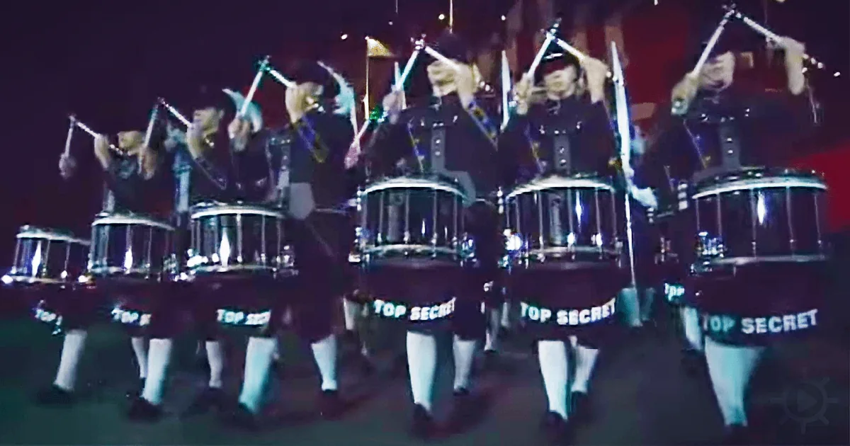 A group of drummers in uniform play in formation, their drums labeled "TOP SECRET."
