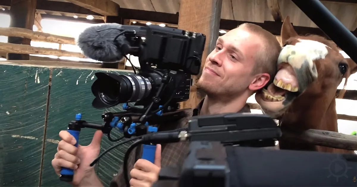 A man holds a professional camera, filming a horse with a funny expression.