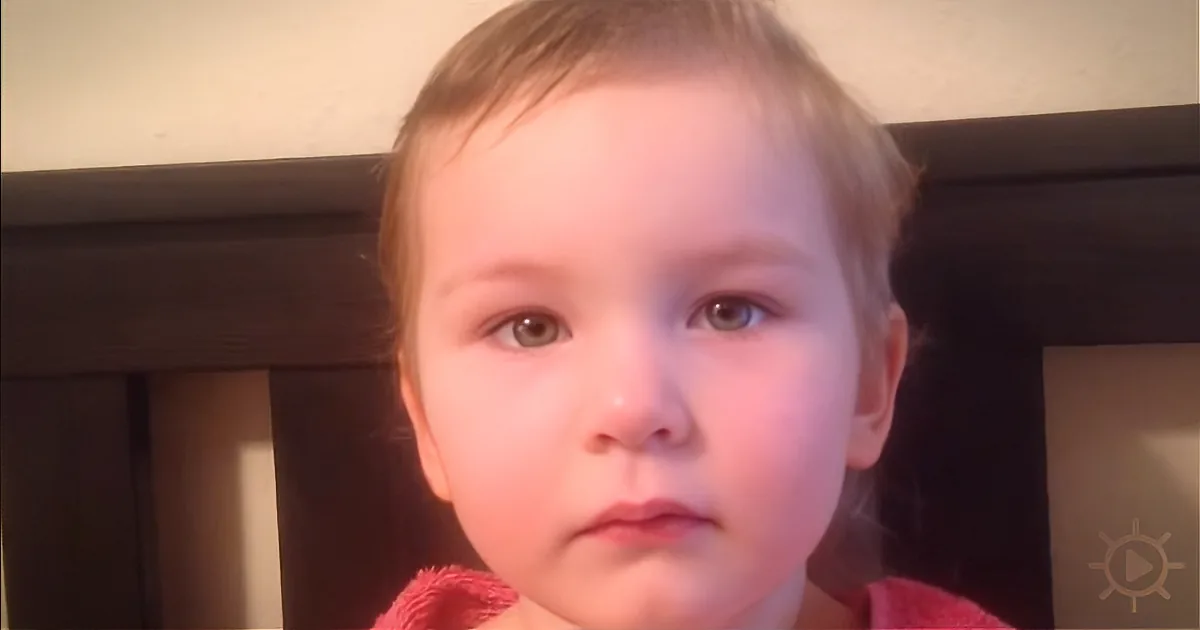 A young child with light hair and a red garment, looking directly at the camera.