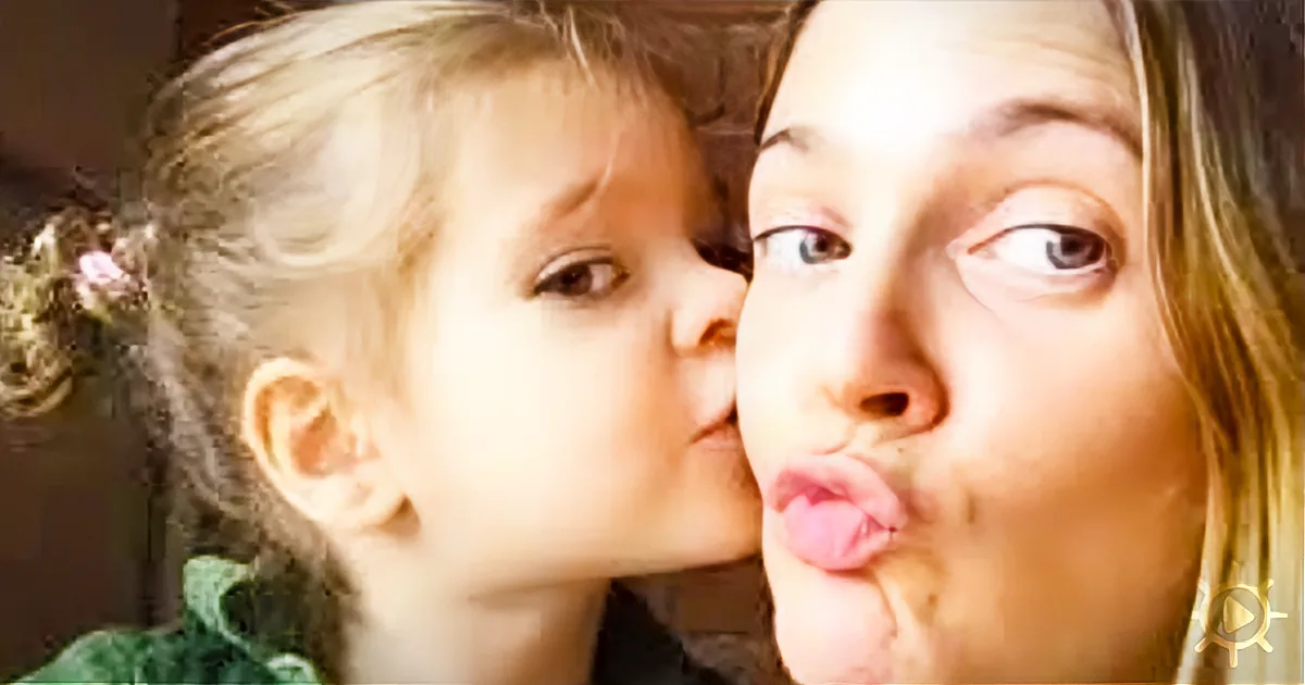 A young girl kisses a woman on the cheek while both make playful faces.