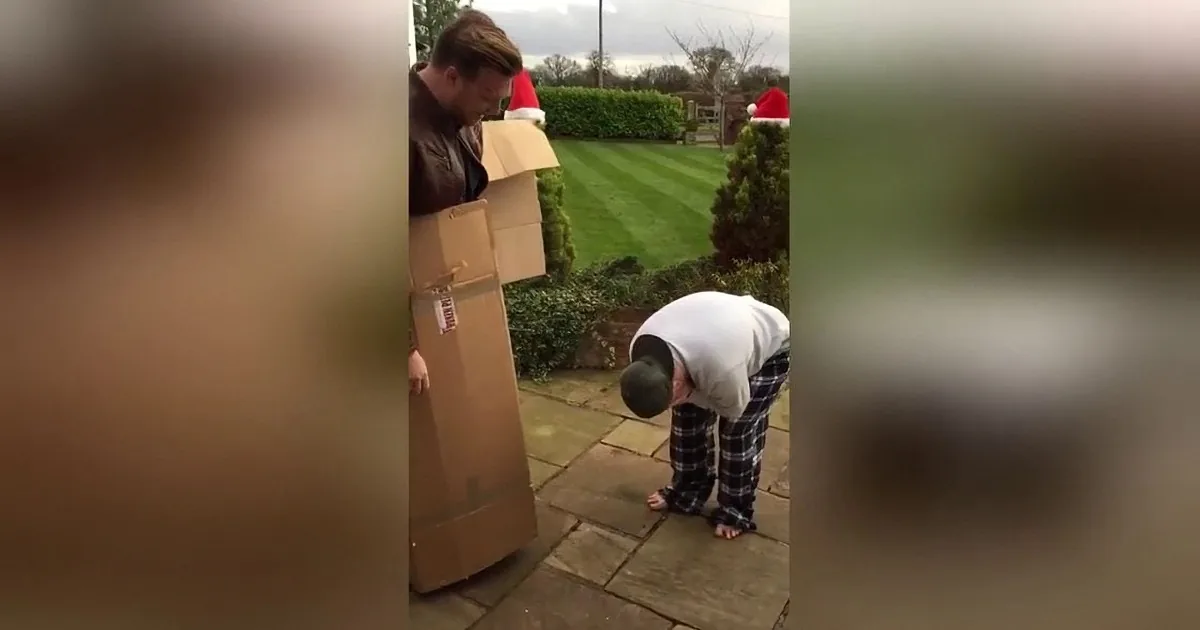 A man in a brown jacket hides behind cardboard boxes as a child in pajamas crouches nearby.