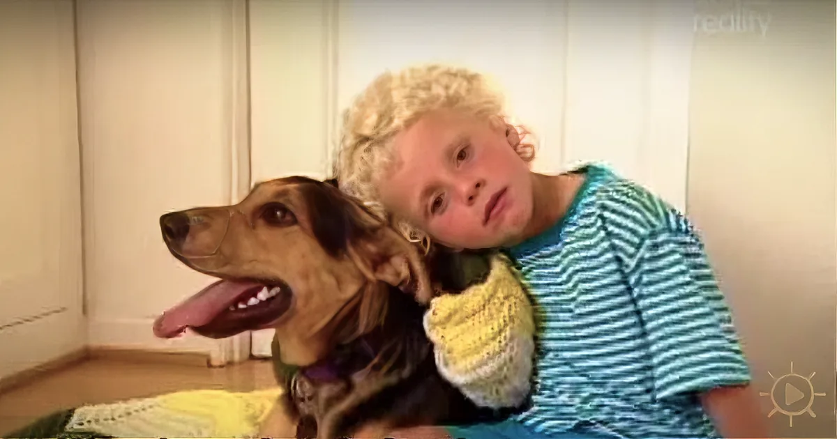 A child with blonde hair hugs a brown dog with a happy expression.