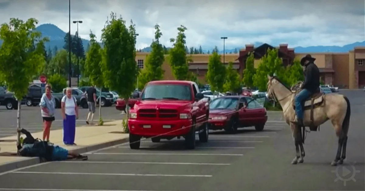 A man on horseback in a parking lot, pulling a rope, with a red truck and people nearby.