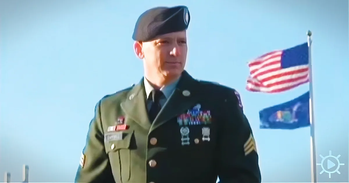 A soldier in a green uniform stands in front of an American flag, wearing a beret and medals.